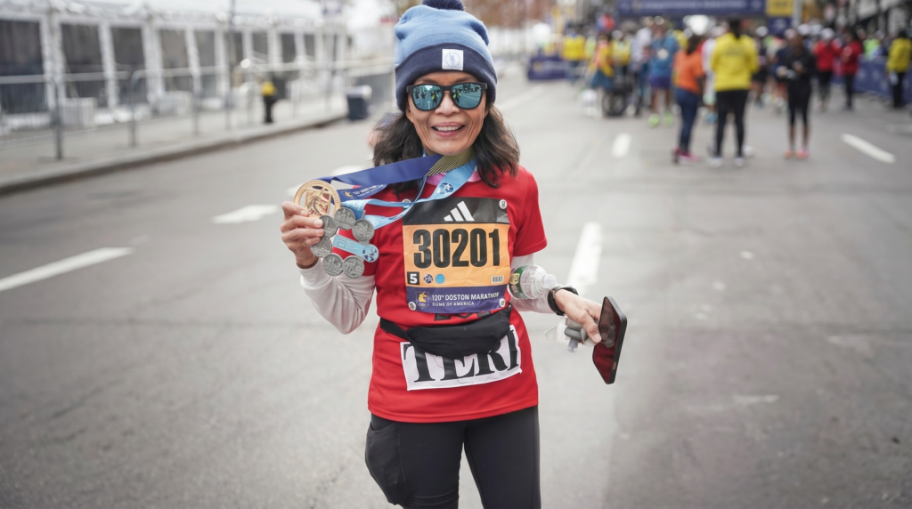 Runner holding Boston Marathon medal and Abbott World Marathon Majors six-star medal on Boylston Street after the finish.